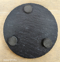 Load image into Gallery viewer, Round black slate coaster with three raised circular pads on a wooden surface