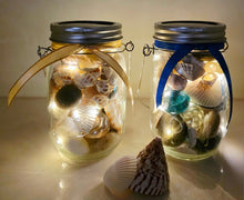 Load image into Gallery viewer, Jars filled with shells, pebbles and coloured glass stones. Lit up with lid and carry handle. Blue decorative ribbon