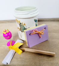 Load image into Gallery viewer, white painted jar with butterfly detail, lilac and yellow paper scrapbook, brown pencil, pink toy and a white rolled up note tied with yellow ribbon