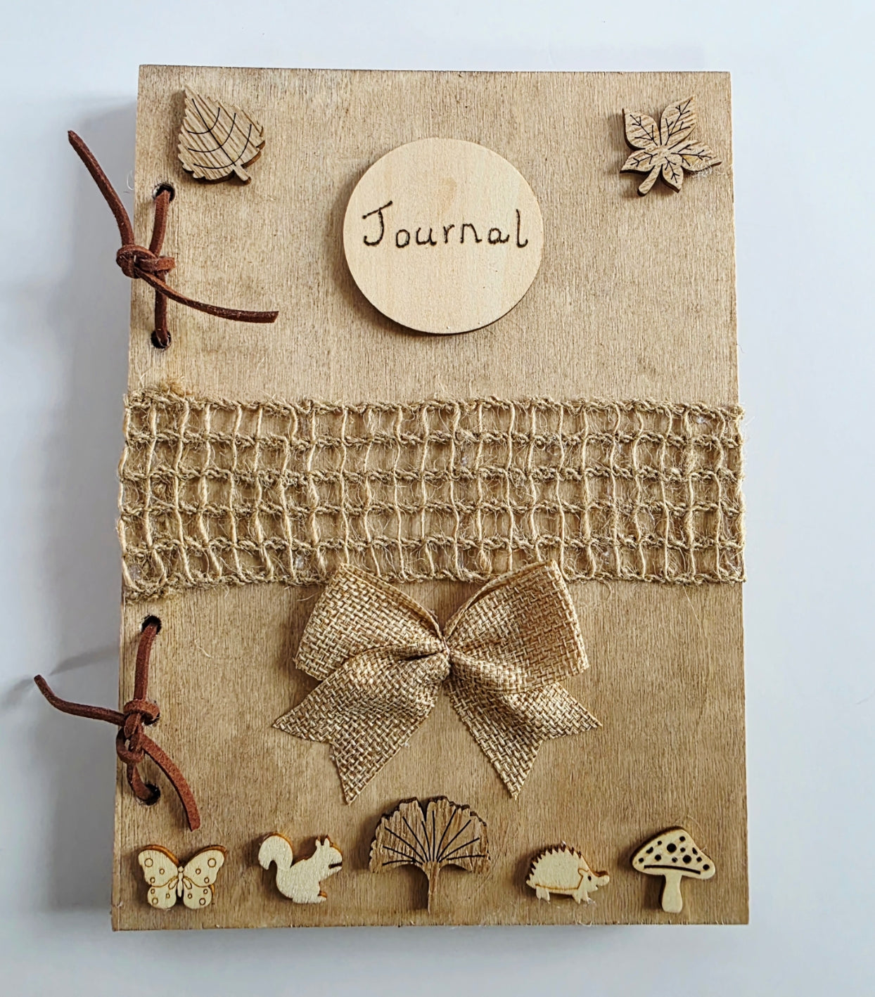 handmade rustic journal with wooden outercovers embellished with woodland creatures and wooden leaves. Burlap mesh decoration across the front, bound with brown suede, decorative hessian bow