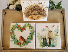 Load image into Gallery viewer, Three nature-themed prints featuring a hedgehog, robin, and lamb on a wooden surface with floral decorations.