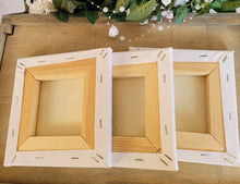 Load image into Gallery viewer, Three square canvases shown from the back/underside showing the wood frames and staples in the canvas, on a wooden surface.