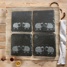 Load image into Gallery viewer, Four slate coasters with sheep illustrations on a wooden board.