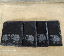 Load image into Gallery viewer, Four black slate coasters with white sheep illustrations on a wooden surface.