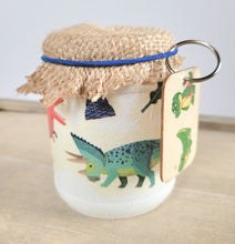 Load image into Gallery viewer, white painted jar with Dinosaur detail, wooden keyring with green Dinosaur on it, brown hessian lid secured with a blue elastic band