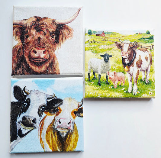 set of three decoupage pictures on stretched white canvas. 1. A highland cow. 2. A black and  white cow and a brown and white cow looking nosey. 3. A sheep, pig and cow standing in a meadow