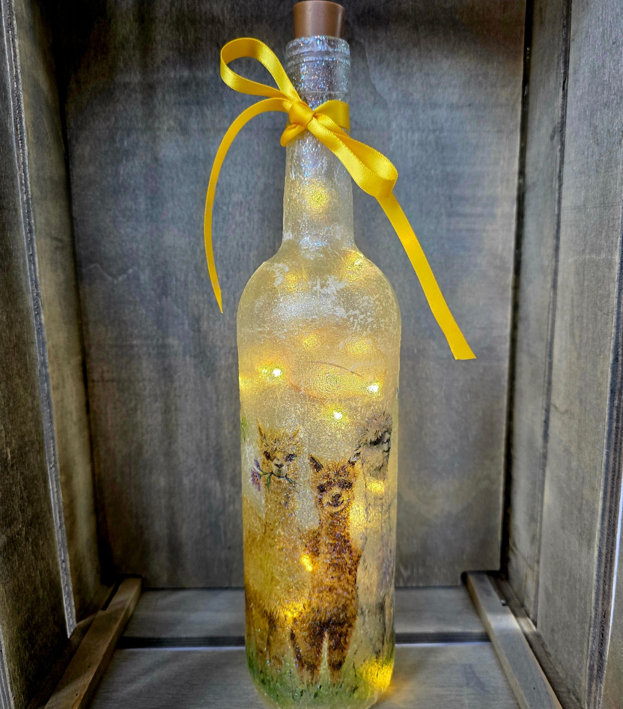 Decorative bottle with Alpaca design LED lights and a yellow ribbon on a wooden surface.