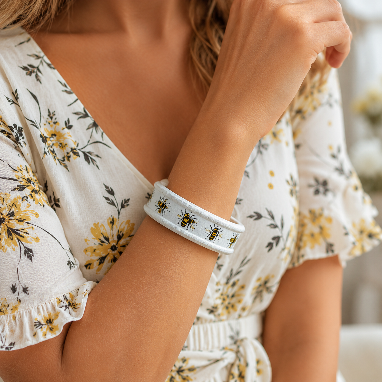 A close-up of a woman wearing a white wooden bangle with yellow and black bumblebees pattern, paired with a white floral dress