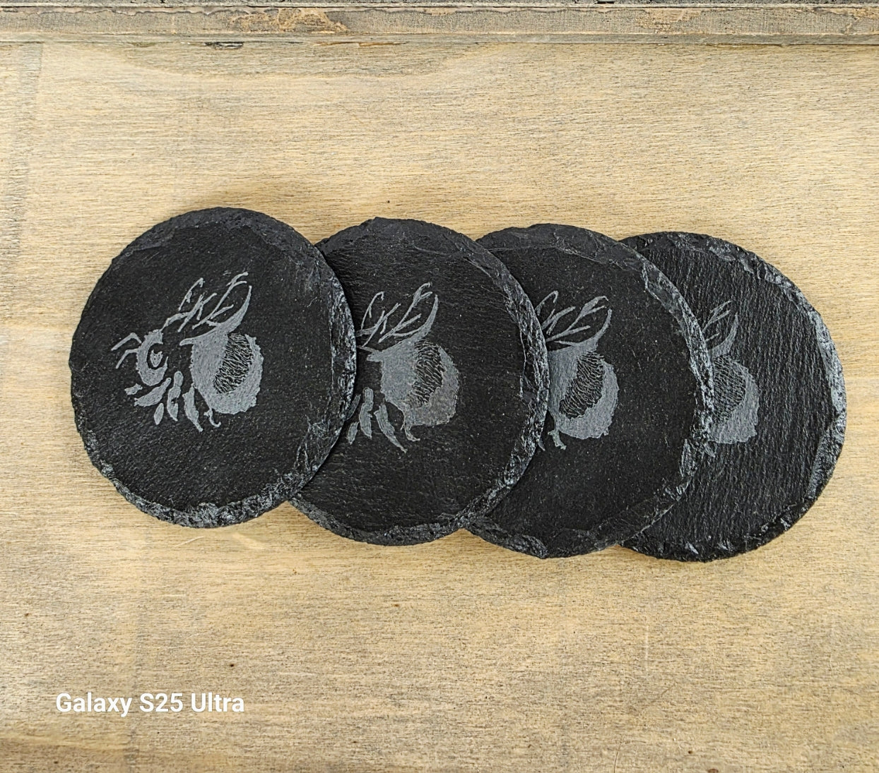 Set of four black slate coasters with Bee design on a wooden surface