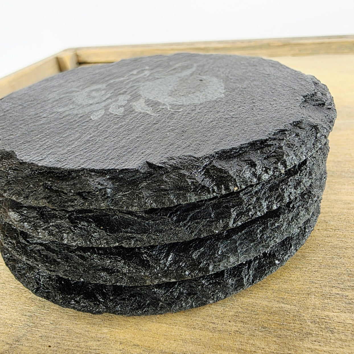 Stack of round black slate coasters on a wooden surface