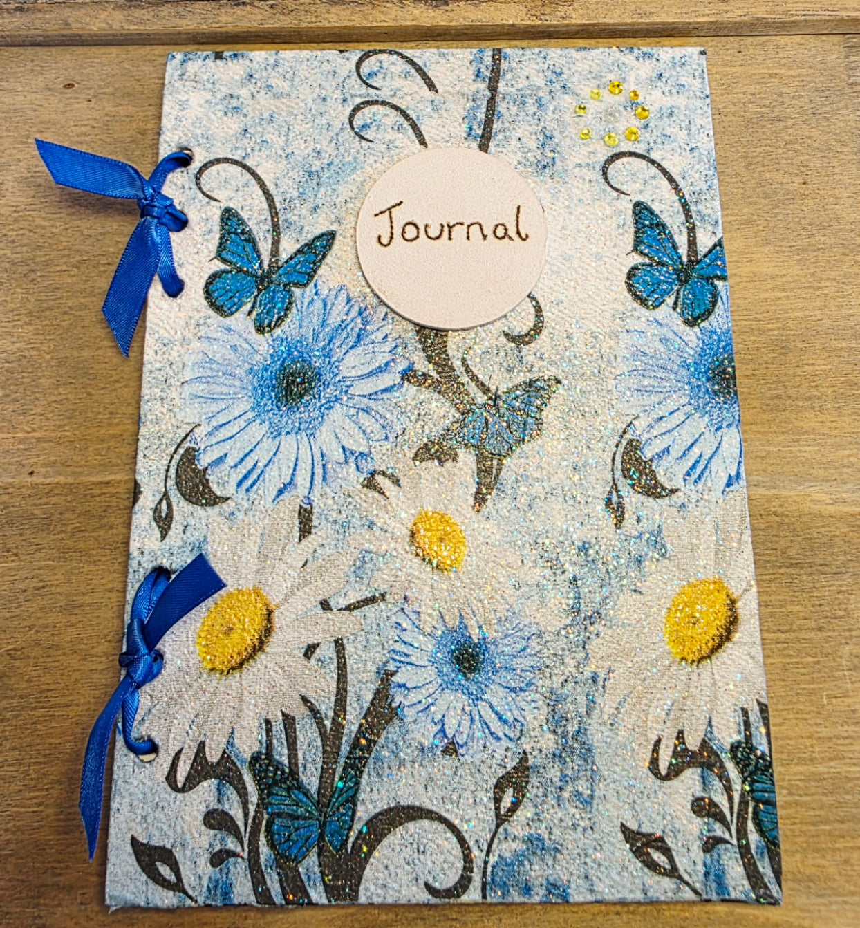 decoupage Journal with blue floral and butterfly  design and blue ribbons on a wooden surface