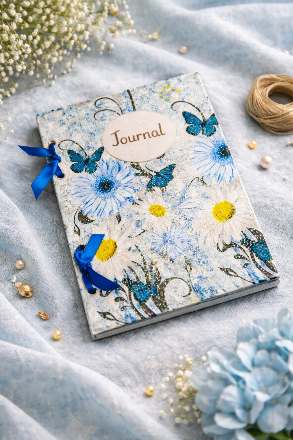decoupage Journal with blue floral and butterfly  design and blue ribbons on a wooden surface. soft fabric background