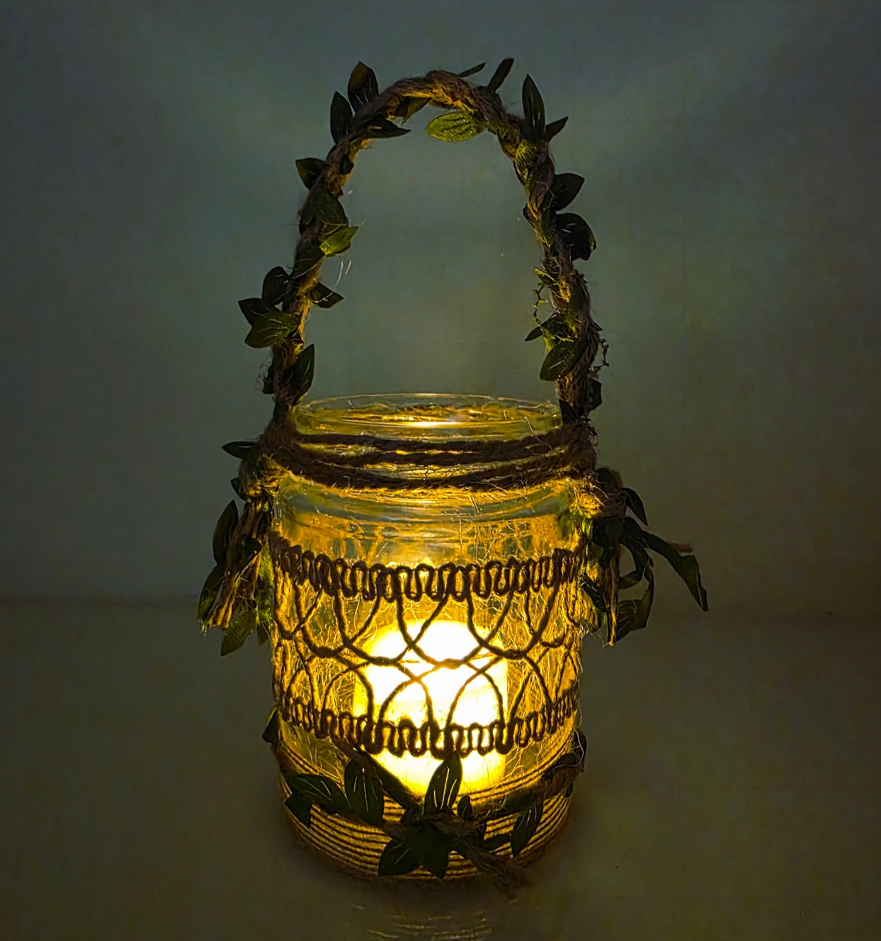 Decorative lantern with leaf-like handle and design on a plain background. Lit up with flameless candle