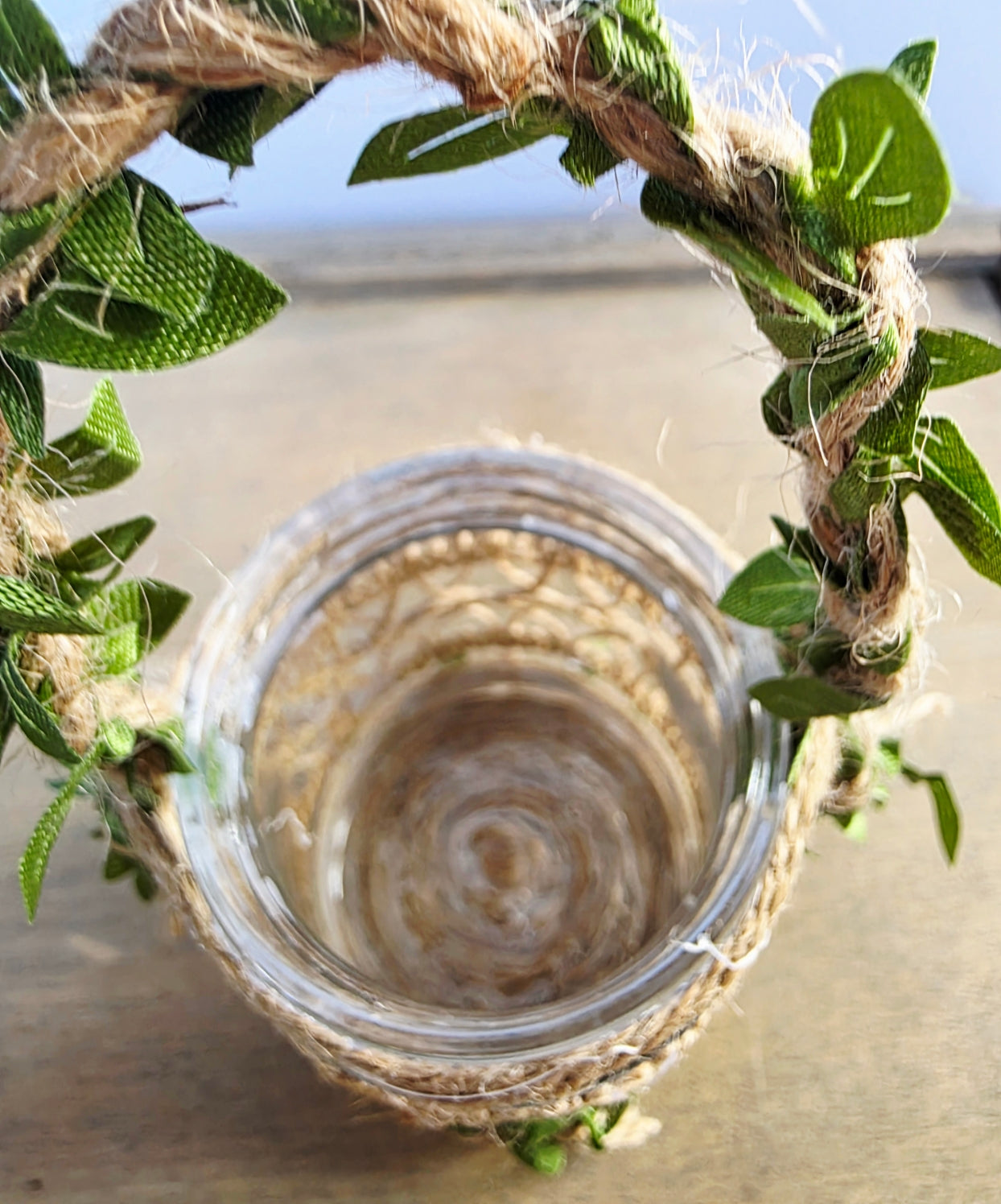 Glass jar with a decorative handle made of green leaves and twine against a light  background. Showing empty inside of jar