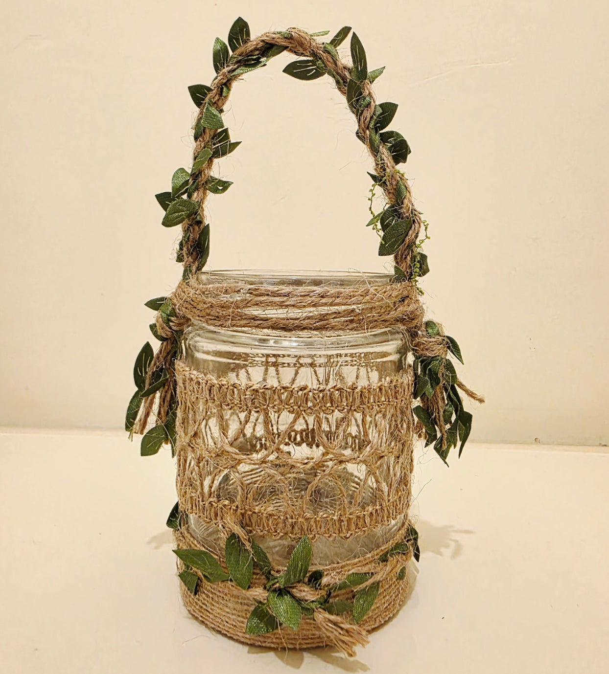 Decorative glass jar with jute wrap and greenery on a beige background