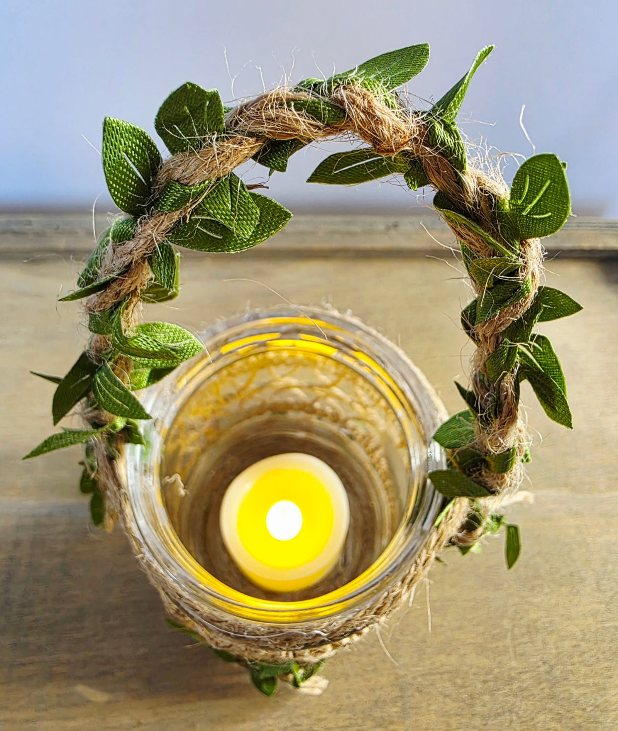 Flameless Candle in a glass jar wrapped with twine and green leaves on a neutral background