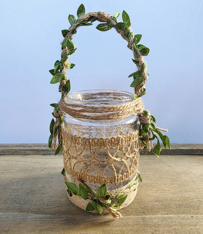 Decorative glass jar with Burlap decoration and green leaves on a wooden surface with a plain background