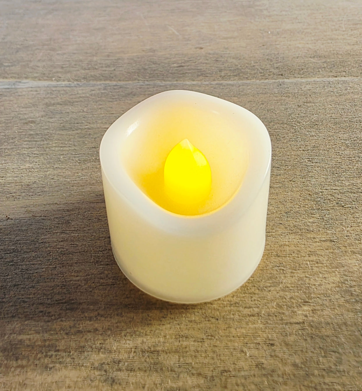 White LED candle with a yellow flame on a wooden surface