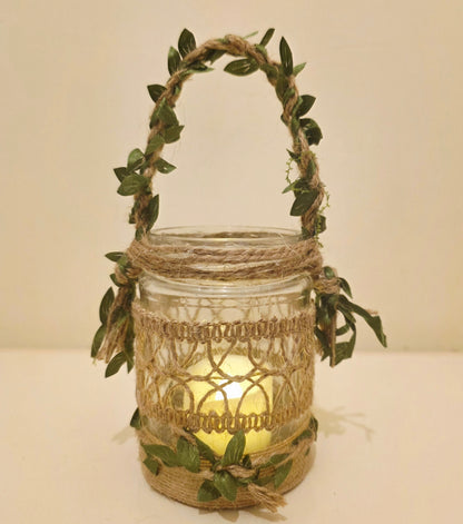 Decorative lantern made from a glass jar, burlap twine wrapping, and green leaves  on a plain background. Flameless candle lit up inside