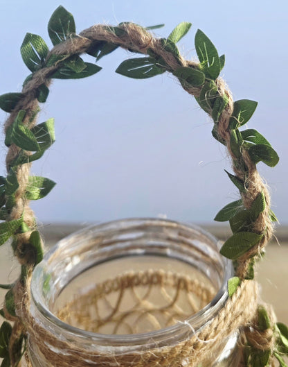 Glass jar with a decorative handle made of green leaves and twine against a light  background