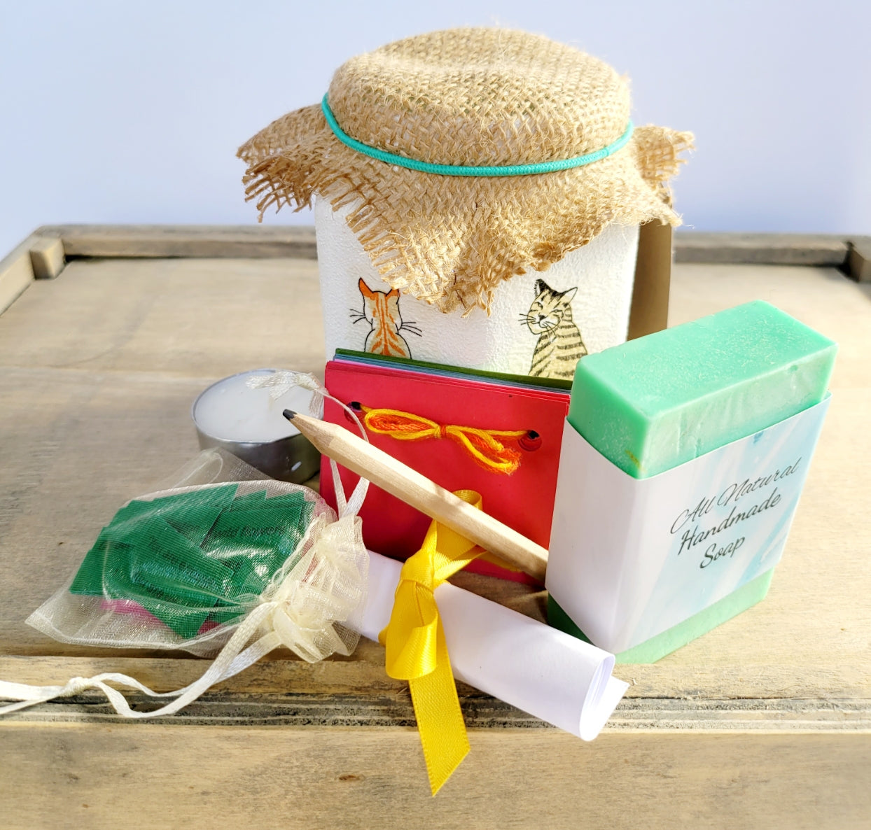 white jar with a green bar of soap, tealight candle, paper scrapbook, brown pencil and small pale organza bag with green paper quotes, brown hessian lid