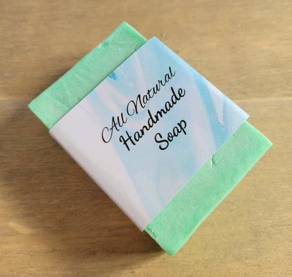 rectangular shaped light green coloured bar of soap with a blue cardboard band around it saying All natural handmade soap