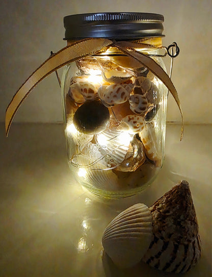 Jar filled with shells, pebbles and coloured glass stones. Lit up with lid and carry handle. gold decorative ribbon