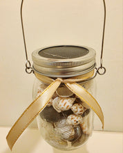 Load image into Gallery viewer, Glass jar with shells and a gold ribbon on a beige background. jar has metal carry handle
