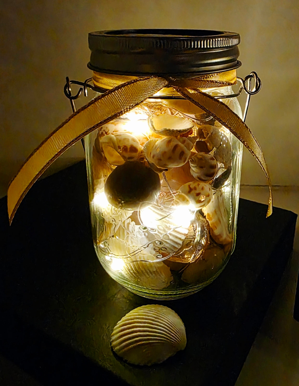 Decorative jar with seashells and LED lights on a dark surface