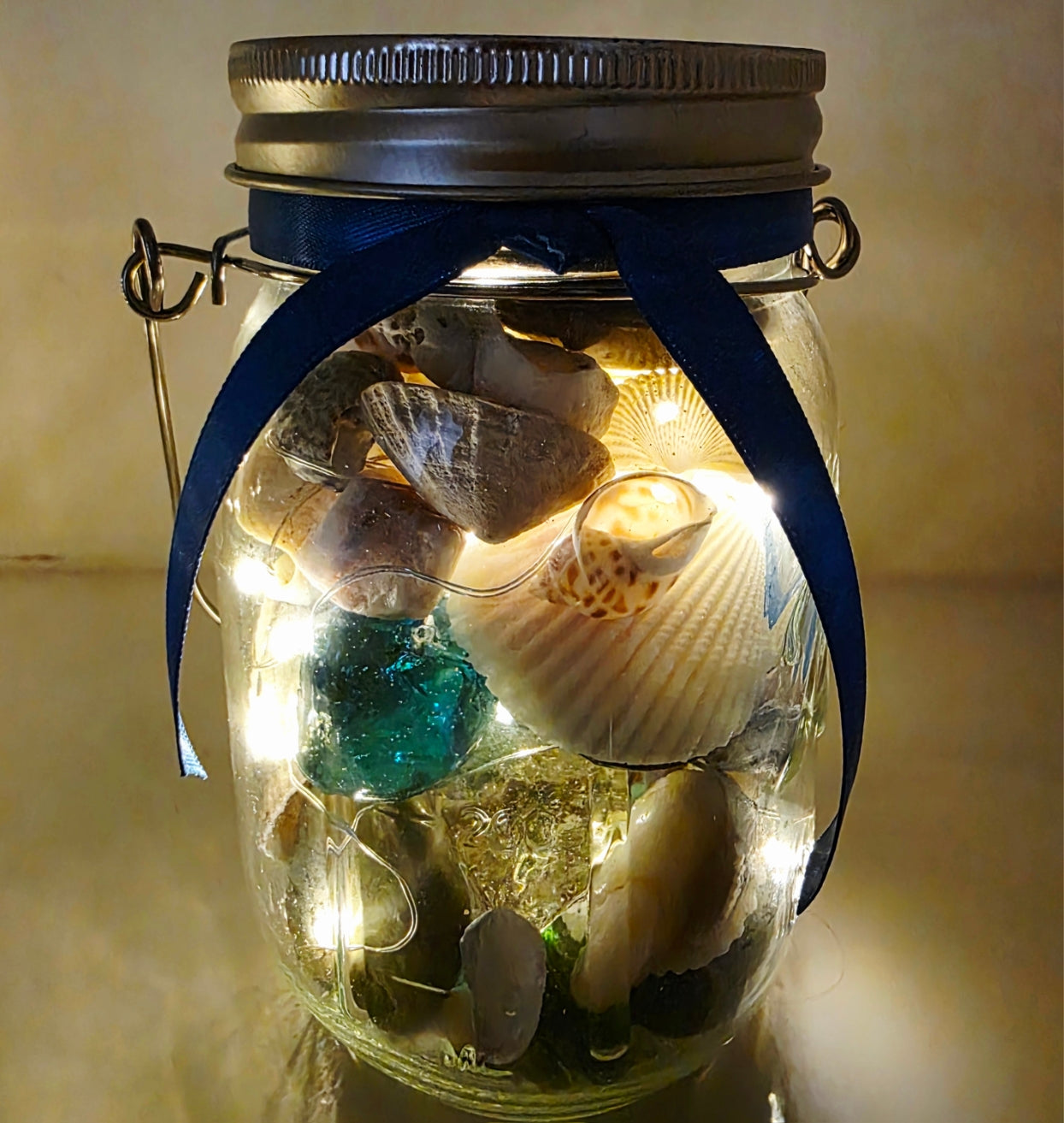 Decorative jar with lights, shells, and stones on a neutral background. Blue ribbon