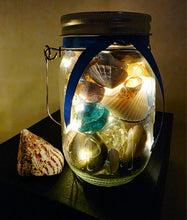 Load image into Gallery viewer, Jar filled with shells, pebbles and coloured glass stones. Lit up with lid and carry handle. Blue decorative ribbon
