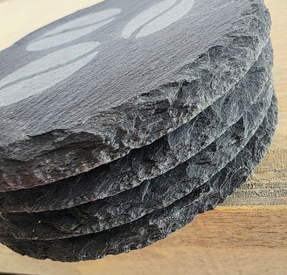 Stack of slate coasters on a wooden surface. Coffee bean design n the top