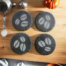 Load image into Gallery viewer, Four round, black slate coasters with coffee bean design on a wooden surface.
