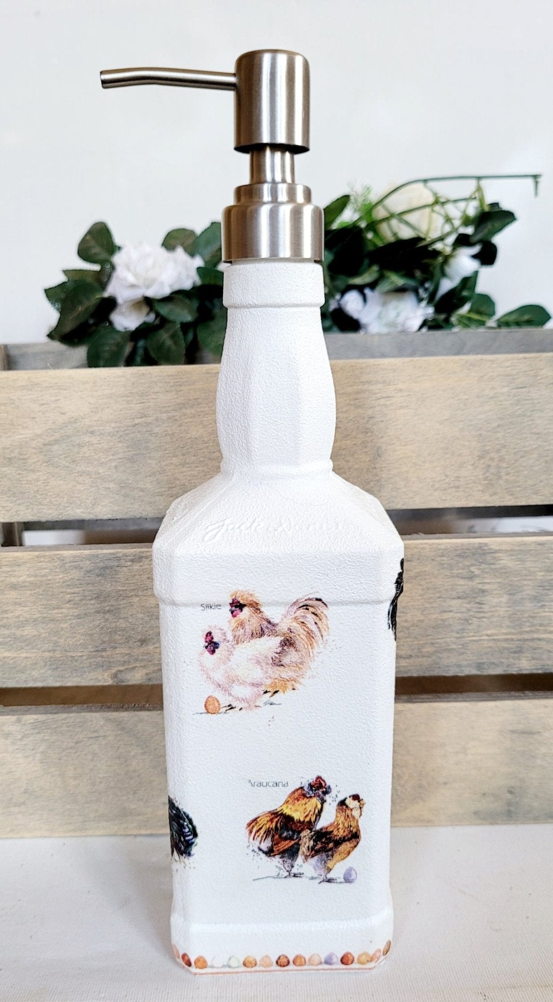 Jack daniels shaped bottle, painted white with chickens detailing around the sides, eggs around the edge at the bottom. Silver pump head