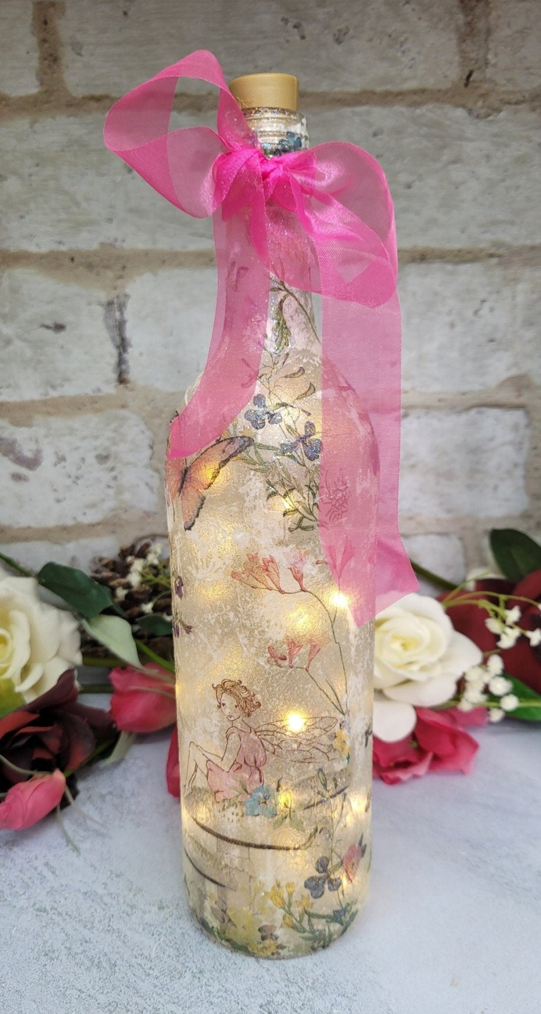 Decoupage Fairy bottle lamp - Lit up standard wine bottle with Fairy and flower butterfly detailing. Pink organza ribbon tied around the neck of the bottle. Cork LED lights