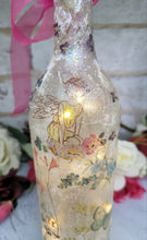 Load image into Gallery viewer, Decoupage Fairy bottle lamp - Lit up standard wine bottle with Fairy and flower butterfly detailing. Pink organza ribbon tied around the neck of the bottle. Cork LED lights
