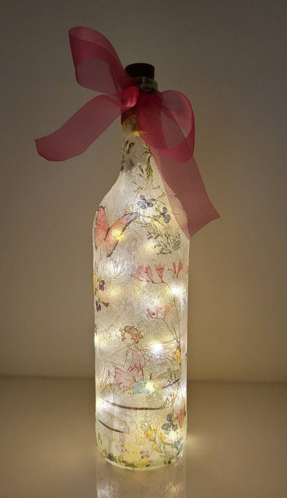 Decoupage Fairy bottle lamp - Lit up standard wine bottle with Fairy and flower butterfly detailing. Pink organza ribbon tied around the neck of the bottle. Cork LED lights