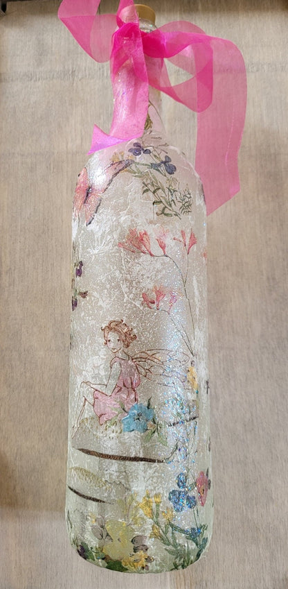 Decoupage Fairy bottle lamp - standard wine bottle with Fairy and flower butterfly detailing. Pink organza ribbon tied around the neck of the bottle. Cork LED lights