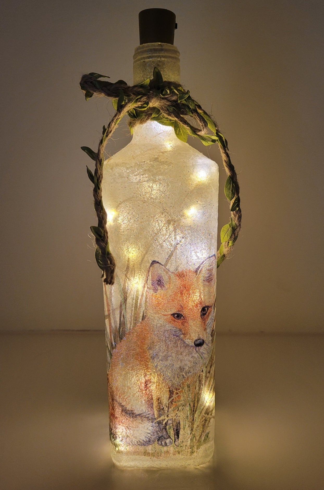 Decoupage Fox Bottle Lamp - Lit up square gin bottle with fox detail and jute twine with leaves wrapped around the neck of the bottle. Cork LED lights