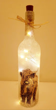 Load image into Gallery viewer, Lit up standard shape wine bottle with highland cow detailing on the front near the bottom. Gold ribbon tied around the neck of the bottle. Cork LED lights
