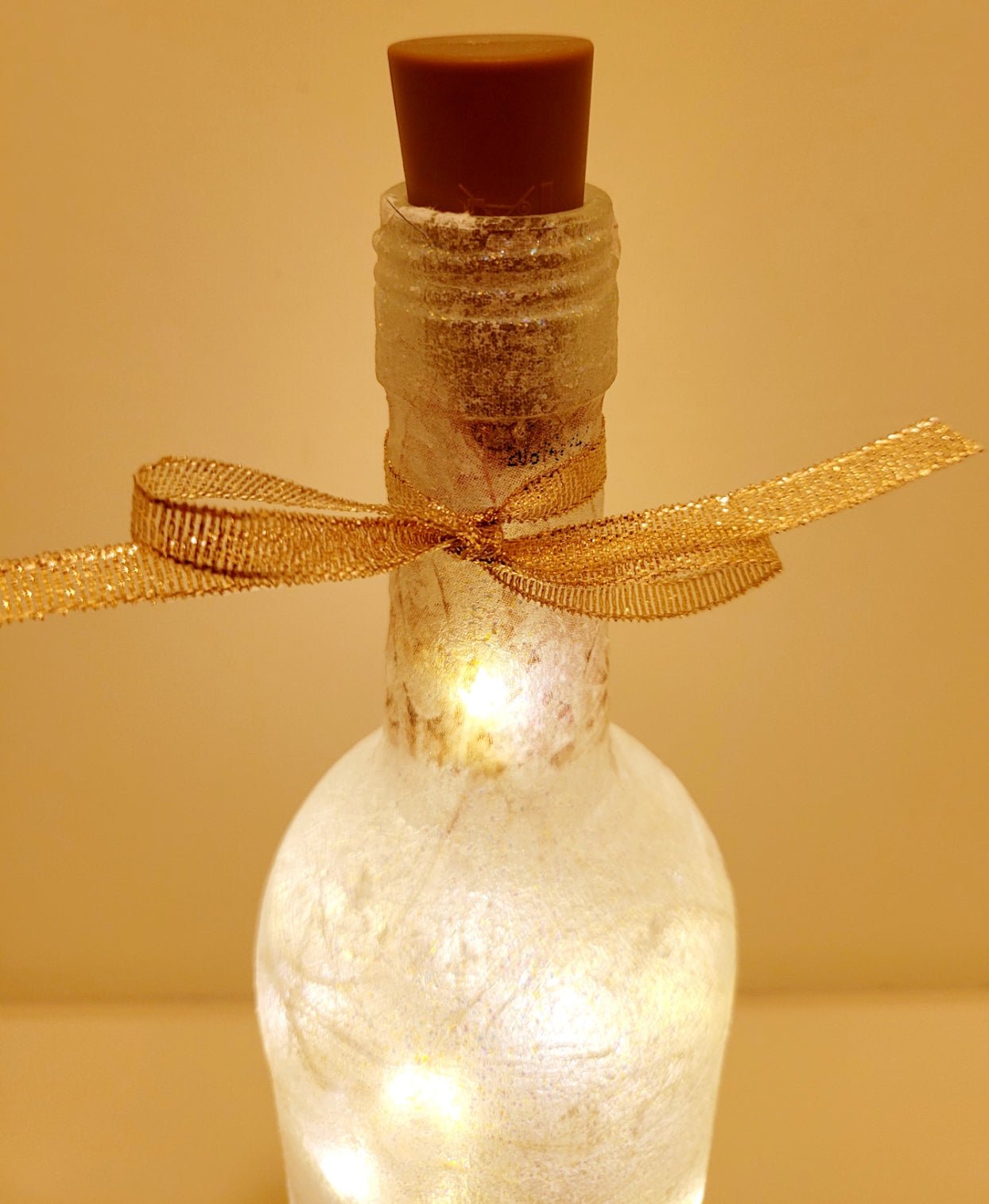Lit up wine bottle with gold ribbon tied around the neck. Brown plastic cork