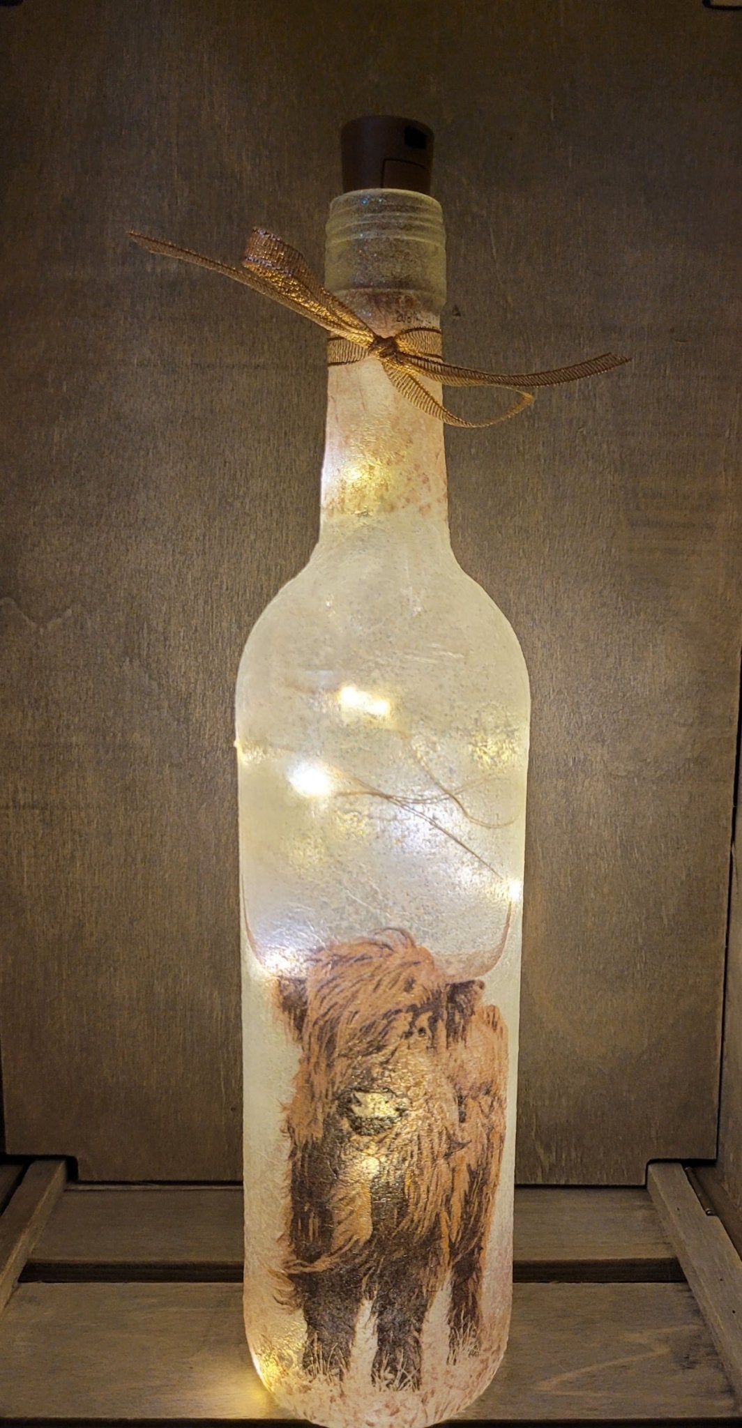 Lit up wine bottl with highland cow detail near the bottom. Gold ribbon tied around the neck of the bottle. ork LED lights