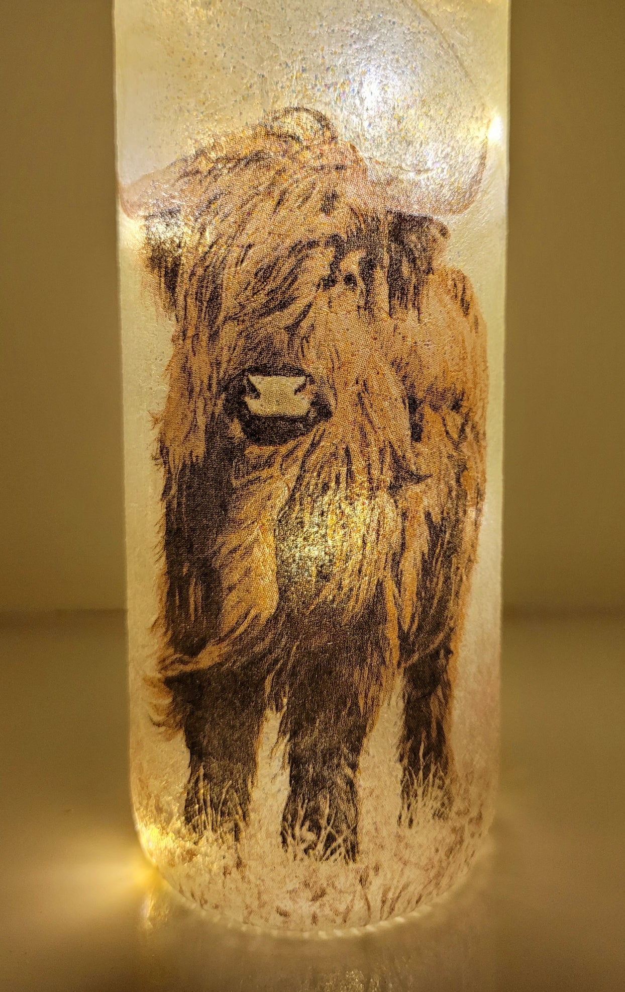 Lit up standard shape wine bottle with highland cow detailing on the front near the bottom. Cork LED lights