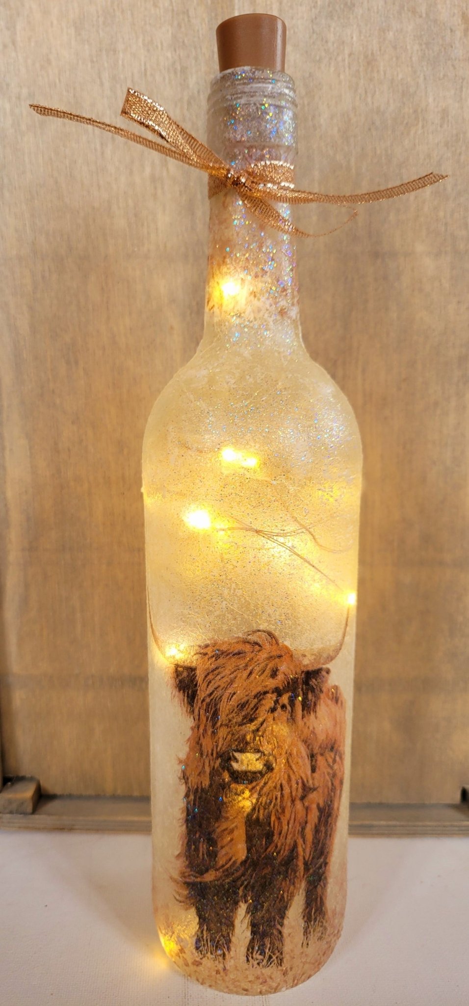 Lit up wine bottle with gold ribbon tied around the neck. Brown plastic cork
