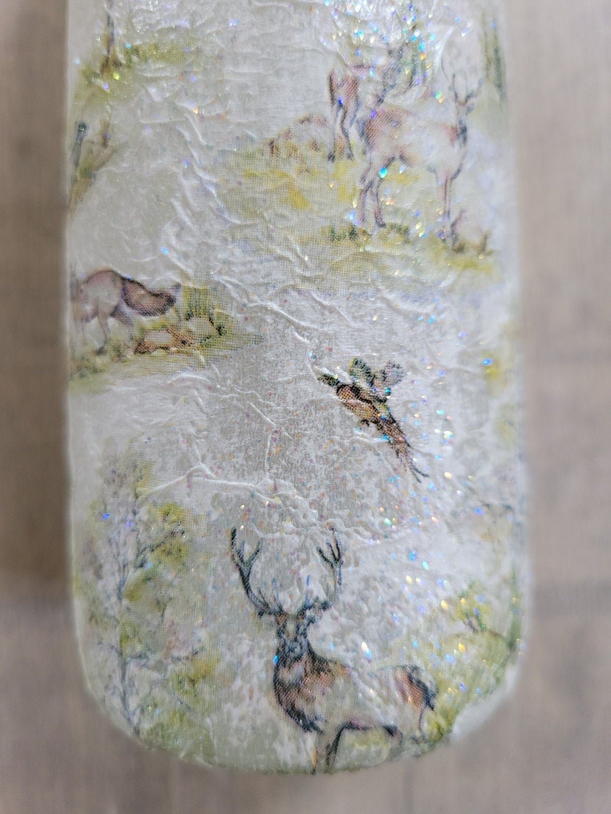 A decorative wine bottle with a woodland scene design. The bottle's surface is textured and covered with images of deer, trees, and other forest animals.