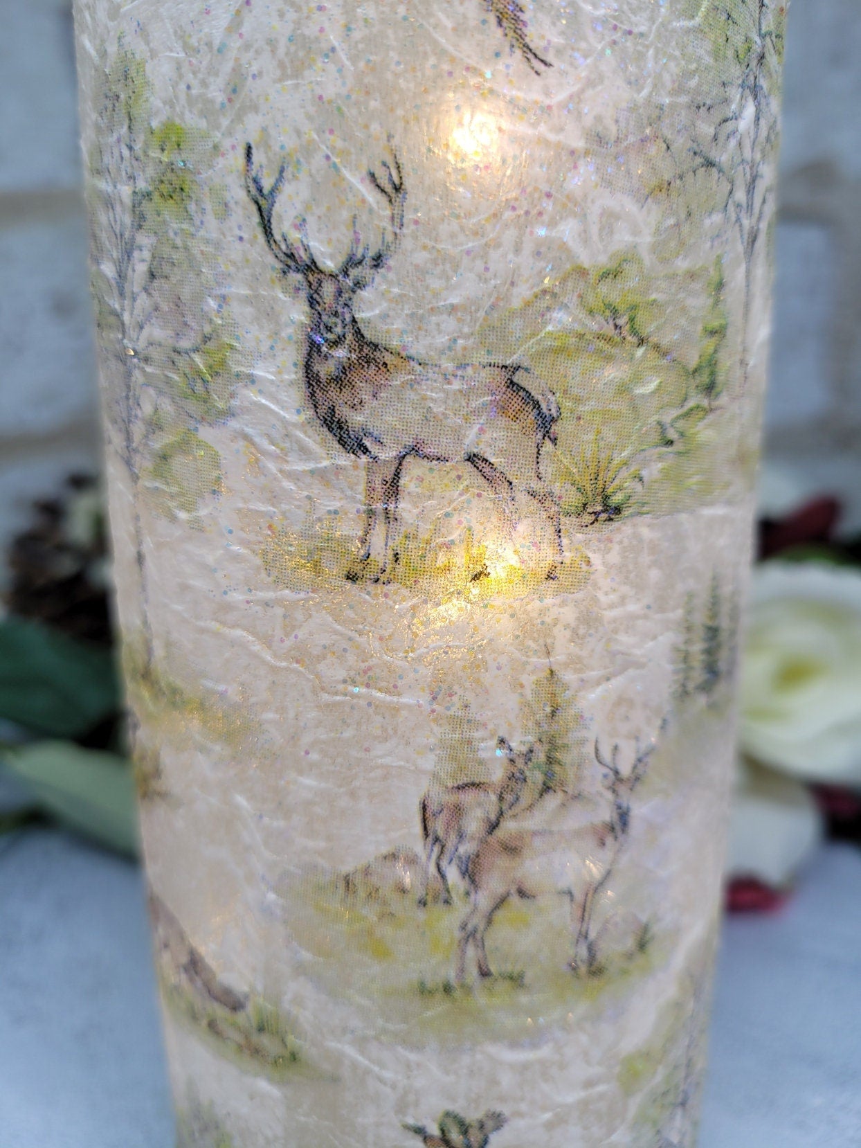 A decorative wine bottle with a woodland scene design. The bottle is illuminated with fairy lights. The bottle's surface is textured and covered with images of deer, trees, and other forest animals.