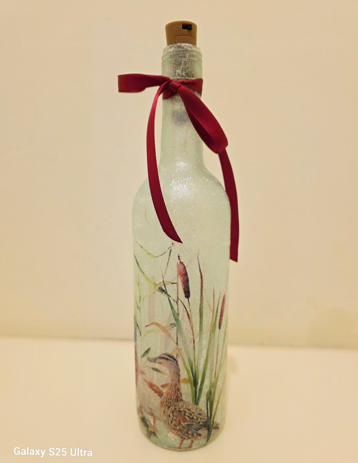Wine bottle with ducks and ducklings on.  with brown cork. Red ribbon embellishment