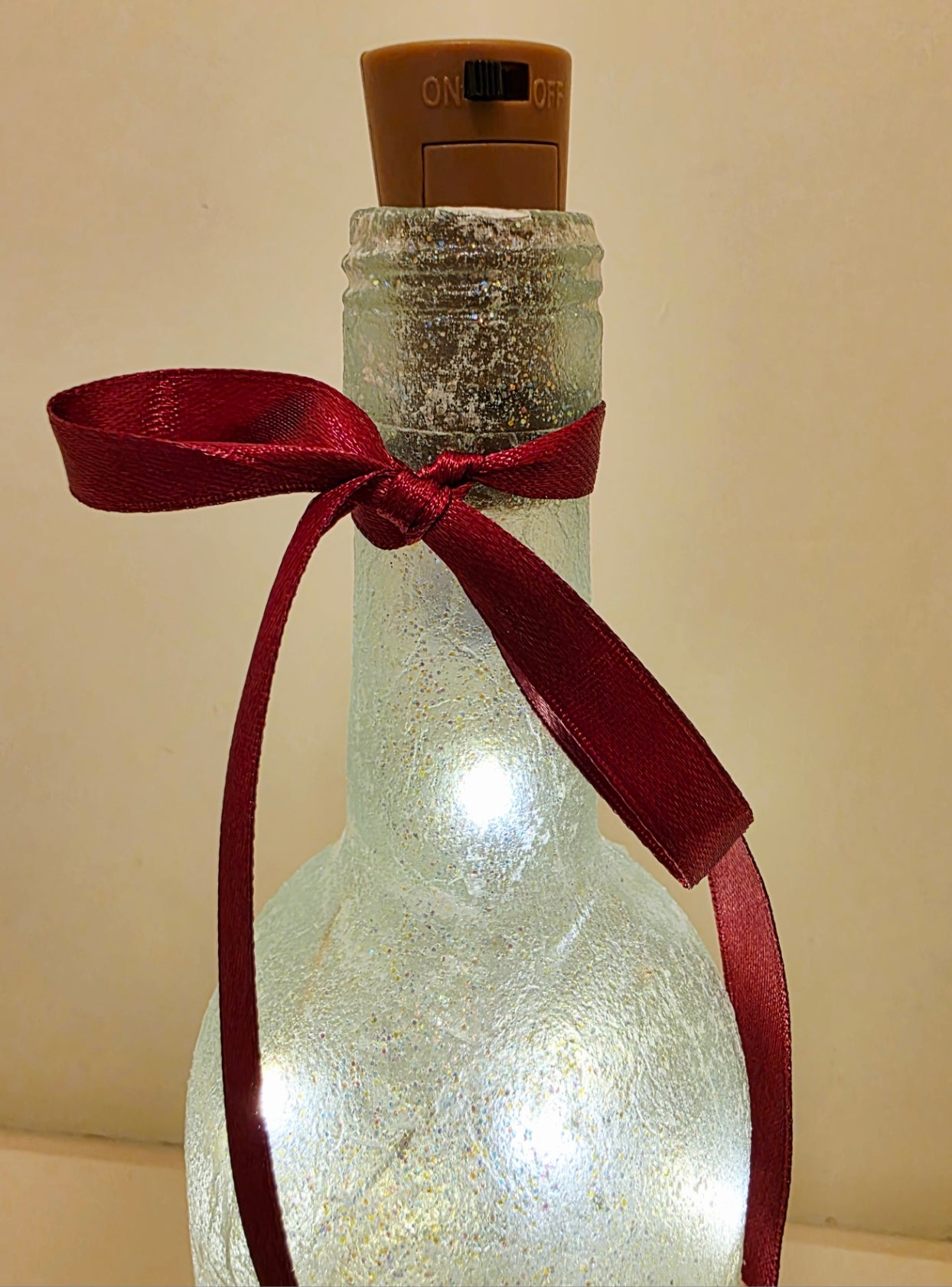 Red ribbon tied around the neck of a wine bottle. Brown cork with black switch