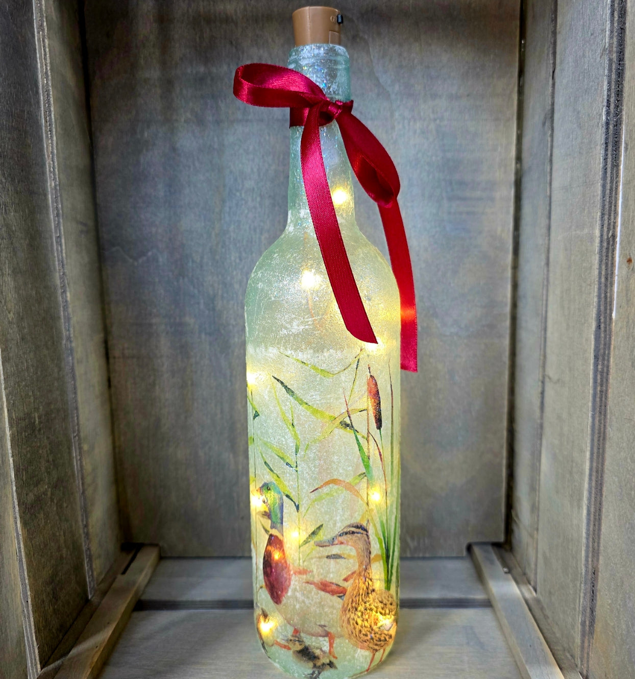 Wine bottle with ducks and ducklings on. Lit up with brown cork. Red ribbon embellishment