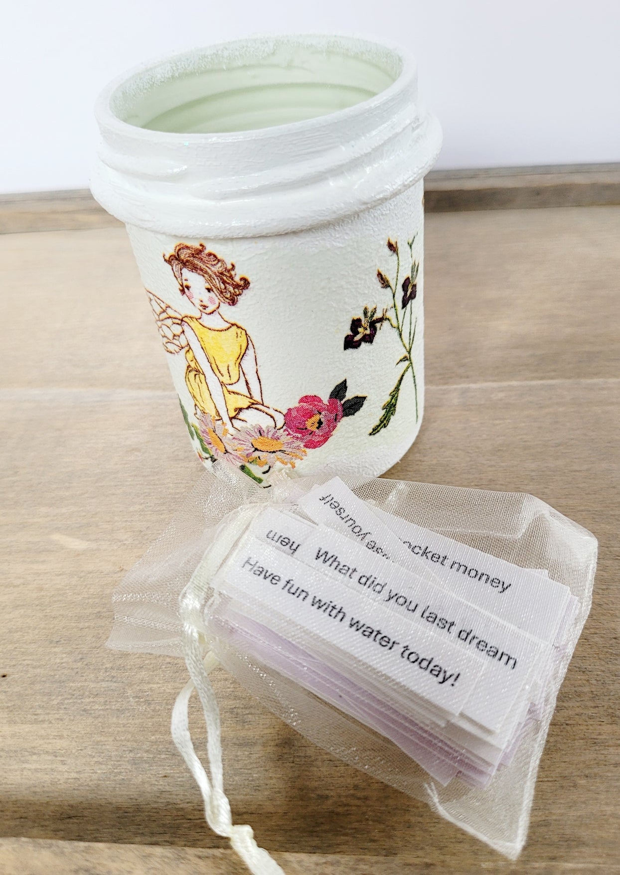 White painted jar with fairy detail, pale organza bag with white paper quotes inside
